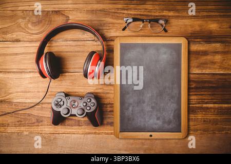 Design plat plat montrant casque, manette de jeu, tableau noir et lunettes sur table en bois Banque D'Images