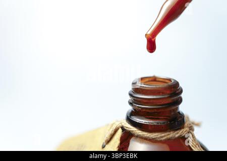 Liquide rouge coulant d'une pipette dans un flacon ambré, créant un contraste visuellement attrayant sur un fond clair Banque D'Images