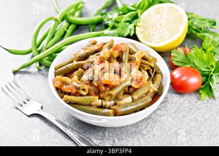 Plat en ragoût arabe plein de haricots verts avec tomates, oignons, épices et citron dans un bol sur fond de table en pierre Banque D'Images