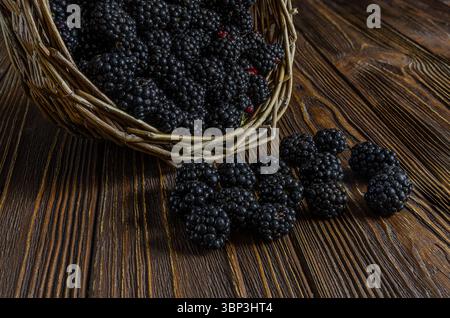 Gros plan de mûres mûres et foncées débordant d'un panier tissé rustique sur une surface en bois riche et texturée, soulignant la fraîcheur et Banque D'Images