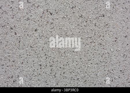 La surface rugueuse mouchetée présente un mélange de tons gris et noirs. La répartition inégale des taches sombres ajoute de la profondeur et de l'intérêt à l'arrière-plan clair. Banque D'Images