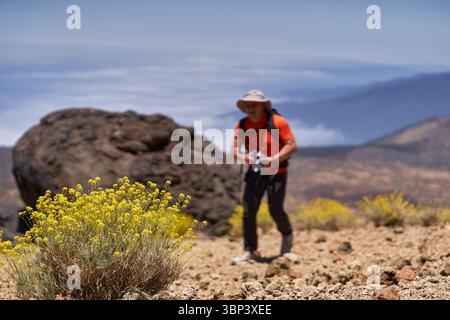 Homme randonnée à travers un terrain volcanique rocheux avec caméra à la main et paysage de montagne en arrière-plan Banque D'Images