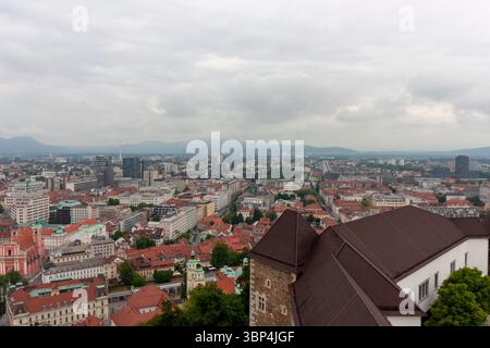 Une vaste vue surélevée capture le paysage urbain de Ljubljana, Slovénie, par temps nuageux. Les toits en tuiles rouges dominent le premier plan, mettant en valeur le Banque D'Images