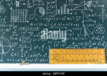 Tableau noir éducatif en classe rempli de formules mathématiques et scientifiques, de graphiques et d'équations, avec un outil de règle de mesure jaune, concept de learni Banque D'Images