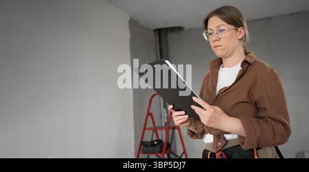 Réparatrice faisant des réparations à domicile des stands de bricolage dans la chambre tenant une presse-papiers Banque D'Images