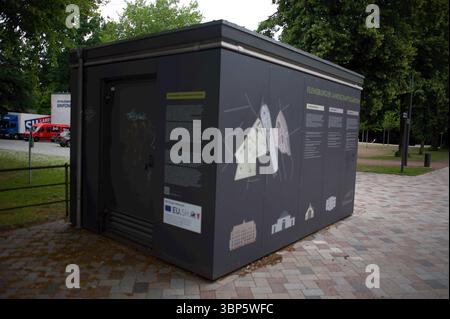 Flensburg, Schleswig-Holstein Kleines Gebäude im Freien, Teil des Projekts Flensburger Landschaftsgärten ehemals Christiansens Gärten auf dem Museumsberg Flensburg. Eine Seite des Gebäudes zeigt eine große Übersichtstafel mit Lageplan und Texten zu den Parkbereichen Christiansenpark, Alter Friedhof und Museumsberg. Die andere Seite ist mit auffälligen, schwarzen Figuren im Stil von Piktogrammen bemalt. DAS Gebäude steht auf einem gepflterten Platz, umgeben von Bäumen und parkenden Autos. Aufnahme vom 06.07.2025, Flensbug, Westliche Höhe. *** Flensburg, Schleswig Holstein petit bâtiment extérieur Banque D'Images