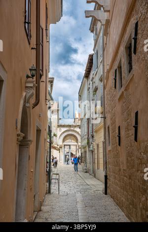 Porec, Croatie - 21 mai 2025 : étroite rue pavée dans la vieille ville méditerranéenne historique avec des bâtiments en calcaire et une ancienne arche en pierre. Touristes Banque D'Images