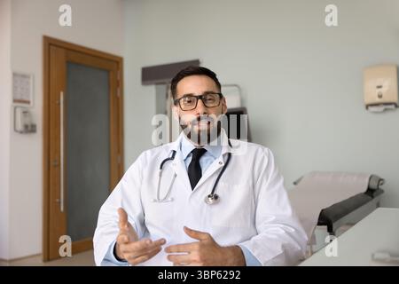 Beau médecin latin positif donnant une consultation en ligne Banque D'Images