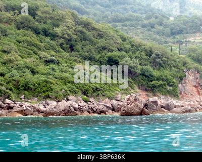 Les eaux turquoises se tapissent doucement contre un rivage accidenté orné de verdure luxuriante et de formations rocheuses, mettant en valeur la beauté de Montenegros Adriatic Banque D'Images