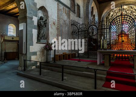 Une vue de l'intérieur de St Mary et St Marc's Minster sur l'île de Reichenau, Bade-Württemberg, Allemagne. La photo montre la zone de l'autel avec une grille en fer forgé ornée, une statue de la Vierge Marie, des peintures murales historiques et un vitrail lumineux ou reliquaire, créant une atmosphère spirituelle dans ce site classé au patrimoine mondial de l'UNESCO. Münsterplatz, Reichenau, Bade-Württemberg, Allemagne Banque D'Images