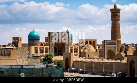 Une vue panoramique de l'architecture historique à Boukhara, Ouzbékistan, avec des structures en dôme avec des toits turquoise et un grand minaret contre un SK bleu Banque D'Images