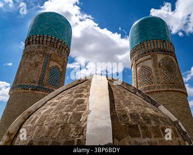 Deux hautes tours au dôme turquoise s'élèvent contre un ciel bleu éclatant avec des nuages moelleux, mettant en valeur des carreaux complexes et une architecture ancienne. Banque D'Images