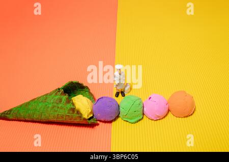 Cuillères de crème glacée multicolores dans un cône de crème glacée vert et jouet de chef sur fond jaune et orange. Couleurs éclatantes Banque D'Images