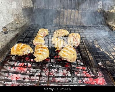 Cuisses de poulet juteuses grillées sur un barbecue au charbon de bois traditionnel. La viande est en train de cuire sur des charbons chauds, avec des marques visibles du gril et de la fumée qui monte, Banque D'Images