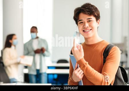 Un homme asiatique souriant prend un masque médical jetable en classe Banque D'Images