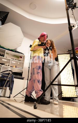 Deux créatifs dans un studio de photographie bien éclairé discutent des détails d'une photo capturée affichée sur l'appareil photo, au milieu de divers équipements pour Banque D'Images