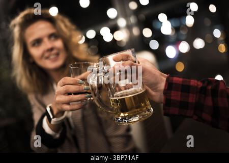 Deux amis tapissent des tasses à bière dans un cadre chaleureusement éclairé, célébrant l'amitié et profitant d'une soirée confortable ensemble. L'arrière-plan est magnifique Banque D'Images