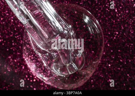 Texture COSMETIQUE liquide compte-gouttes transparente. Macro, gel sérum sur un fond de paillettes roses Banque D'Images