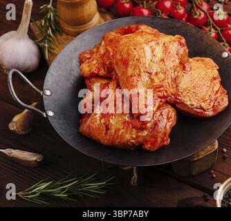 Nourriture, morceaux de poulet mariné juteux assis dans une poêle en fonte, entouré d'ail frais, d'herbes et de tomates cerises, mettant en vedette une gamme vibrante de col Banque D'Images