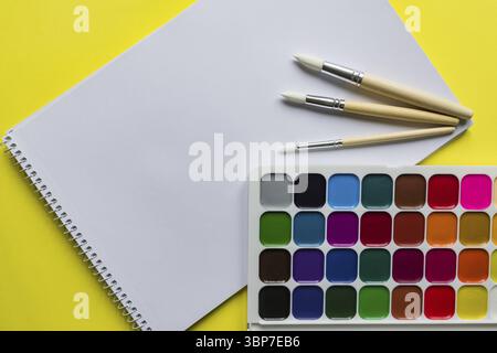 Mise en page créative avec palette d'aquarelle, pinceaux et croquis sur fond jaune. Espace de copie pour le texte Banque D'Images