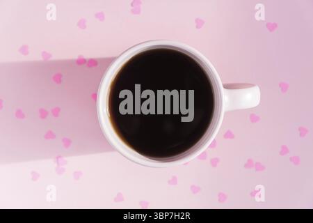 Tasse rose avec du thé noir chaud sur fond rose avec des coeurs en papier dispersés. Concept d'amour et de soins. Espace de copie pour le texte, vue de dessus Banque D'Images