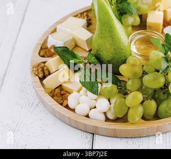 Nourriture, belle planche de charcuterie est disposée sur une table en bois blanc, avec une variété de fromages, raisins frais, une poire et du miel Banque D'Images