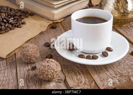 Café frais breveté dans cezve (cafetière turque traditionnelle) boisson du matin dans une tasse blanche à côté des boules de chocolat Banque D'Images