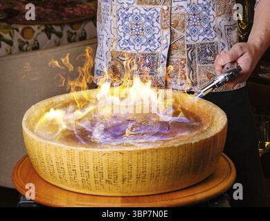 Cuisine, Chef préparant des pâtes dans une roue de fromage enflammée dans un restaurant gastronomique Banque D'Images