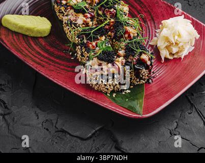 Nourriture, Un plateau de sushis magnifiquement arrangé est servi sur une assiette rouge vif avec divers rouleaux de sushi surmontés d'ingrédients colorés, garnis Banque D'Images