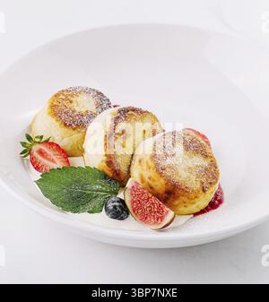 Nourriture, trois crêpes au fromage cottage brun doré garnies de fraises et de menthe sur une assiette blanche Banque D'Images
