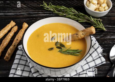 Soupe de citrouille et de carotte avec crème, graines de citrouille, croûtons et bâtonnets de pain grossini sur fond de bois de dar K. Style rustique, mise au point sélective Banque D'Images