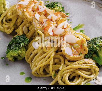 Nourriture, pâtes aux crevettes et brocolis décorés de flocons d'amandes et sauce pesto sur assiette grise Banque D'Images