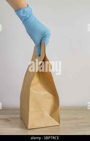 Main de femme dans des gants en latex bleu tenant le sac en papier jetable artisanal pour la livraison. Accouchement sans danger lors de l'isolement du coronavirus Banque D'Images