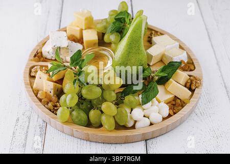 Nourriture, belle planche de charcuterie est disposée sur une table en bois blanc, avec une variété de fromages, raisins frais, une poire et du miel Banque D'Images