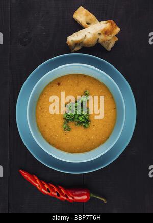 Nourriture, soupe délicieuse servie dans un bol avec de la ciboulette, du piment et du pain sur le côté, tiré d'en haut sur un fond en bois foncé Banque D'Images