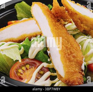 Nourriture, salade fraîche avec des lanières de poulet croustillantes dans un bol à emporter noir gros plan Banque D'Images