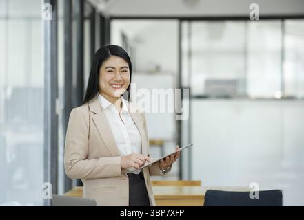Une femme d'affaires professionnelle et confiante souriant à la caméra, debout près de son bureau avec un ordinateur portable dans un bureau moderne Banque D'Images