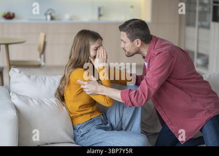 Mari tyran criant et secouant femme en pleurs, se disputant et saisissant ses mains sur le canapé. Querelle familiale, violence domestique et impossibilité d'évasion Banque D'Images