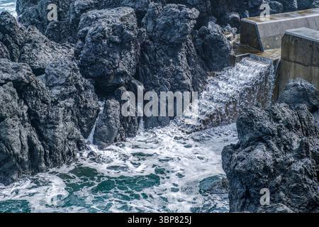 Formations rocheuses volcaniques rugueuses le long de la côte de l'île de Sao Jorge, aux Açores, avec de l'eau moussante de l'océan en cascade dans les piscines naturelles. Falaises accidentées, Banque D'Images