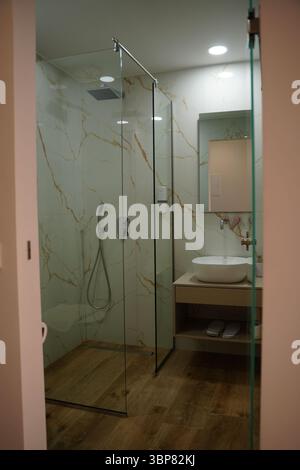 Salle de bains contemporaine avec cabine de douche en verre, élégants murs à motifs en marbre et parquet. Comprend un évier de comptoir élégant et Banque D'Images