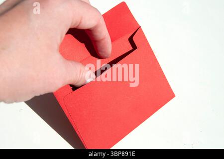 Une main tenant une enveloppe rouge sur blanc. Une main ouvrant une petite enveloppe rouge. Une main avec une enveloppe rouge gros plan. Banque D'Images