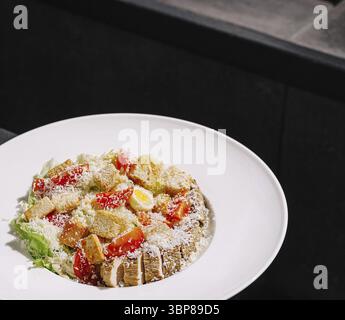 La nourriture, Une salade colorée avec des légumes verts frais, des tomates mûres, des croûtons croustillants et du fromage râpé est magnifiquement présenté dans un b élégant et contemporain Banque D'Images