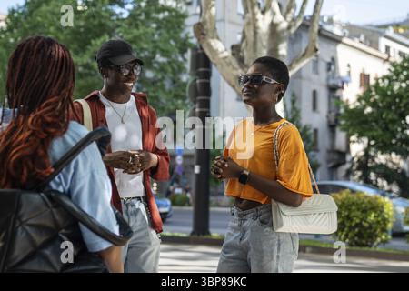 Les étudiants afro-américains satisfaits intéressés qui aiment passer du temps ensemble souriant racontant des histoires debout sur le trottoir. Heureux heureux heureux groupe élégant Banque D'Images