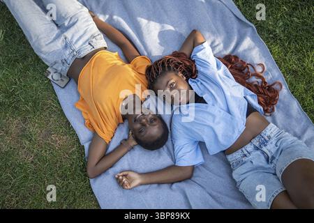 Détendu insouciant couple afro-américain de filles amis se prélassant, couché sur une couverture sur l'herbe dans le parc. Vue de dessus de la femme regardant la caméra. Joie et co Banque D'Images