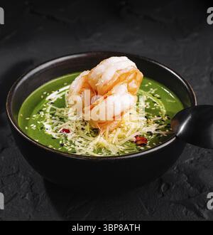 Nourriture, présentation gourmande de soupe de crevettes aux épinards ornée de garnitures dans un bol sombre sur une surface texturée Banque D'Images