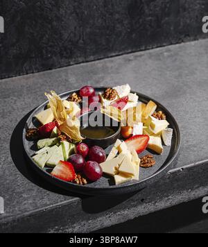Nourriture, Un plat magnifiquement arrangé présente une variété de fromages, des fruits frais comme des raisins et des fraises, et des noix. La présentation artistique sho Banque D'Images