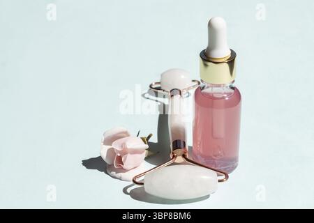 Massage facial à l'huile essentielle de rose cosmétique et à rouleau de quartz rose Pierre Gua-sha pour un massage de beauté du visage à la maison. Soin de la peau et soin du visage conce Banque D'Images