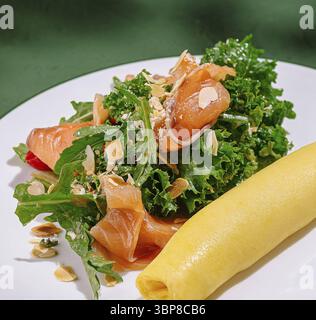 Nourriture, salade colorée avec légumes verts frais, saumon fumé et amandes croquantes. Accompagné d'une omelette roulée douce, ce plat est servi avec élégance Banque D'Images