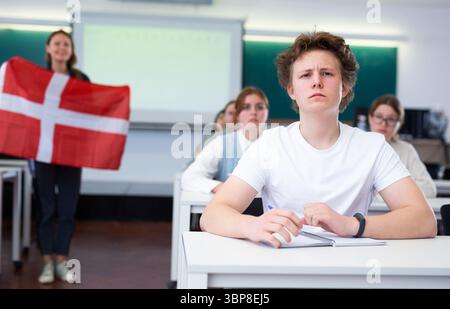 Un enseignant du secondaire parle aux élèves du Danemark et détient un drapeau du Danemark entre les mains. Banque D'Images