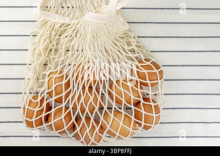 Concept de Pâques. Pas de concept de sac en plastique. Style minimaliste. Sac à provisions en maille beige avec œufs de poulet brun sur fond textile Banque D'Images